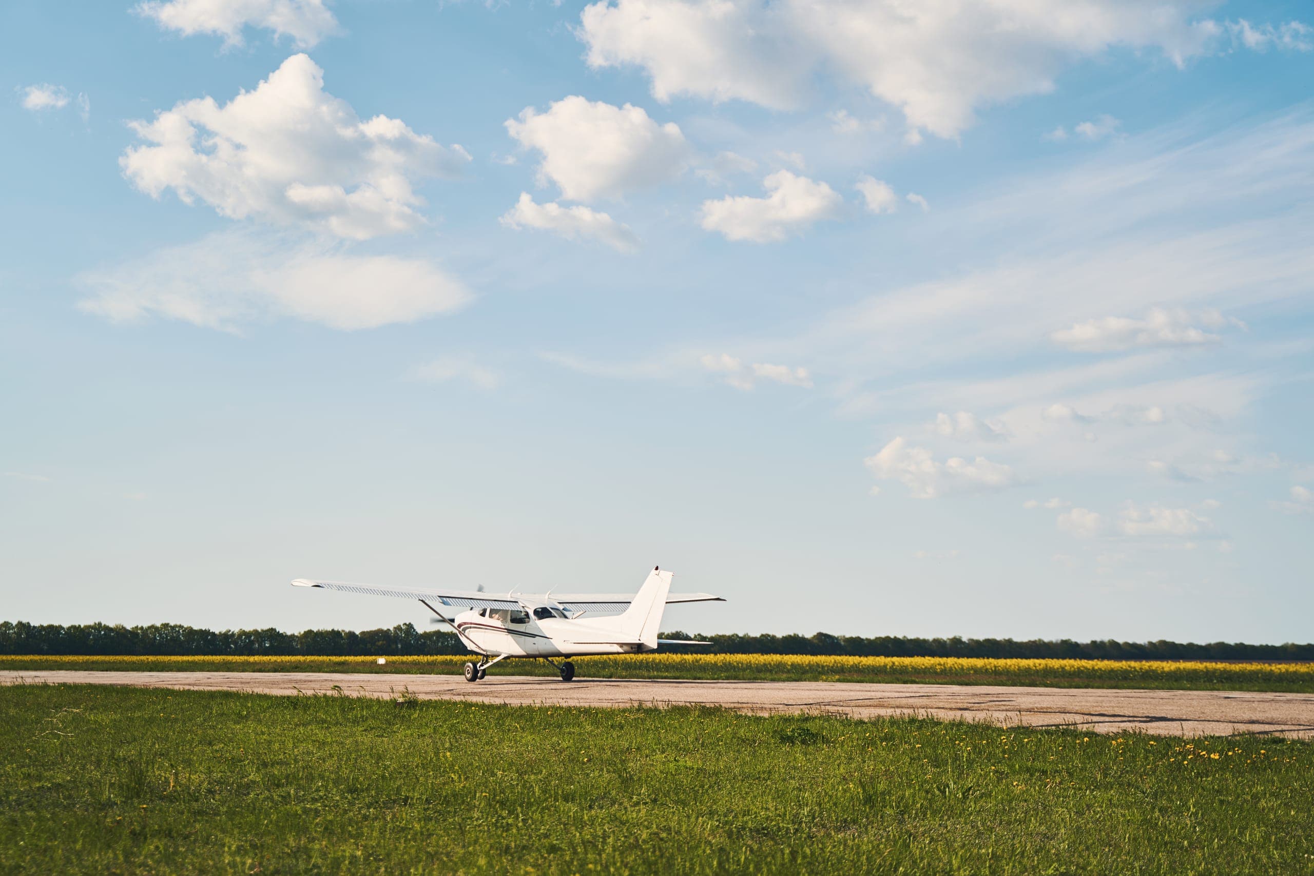 A Cessna 172 on the runway of a small airfield, under a sky with cumulus clouds.
